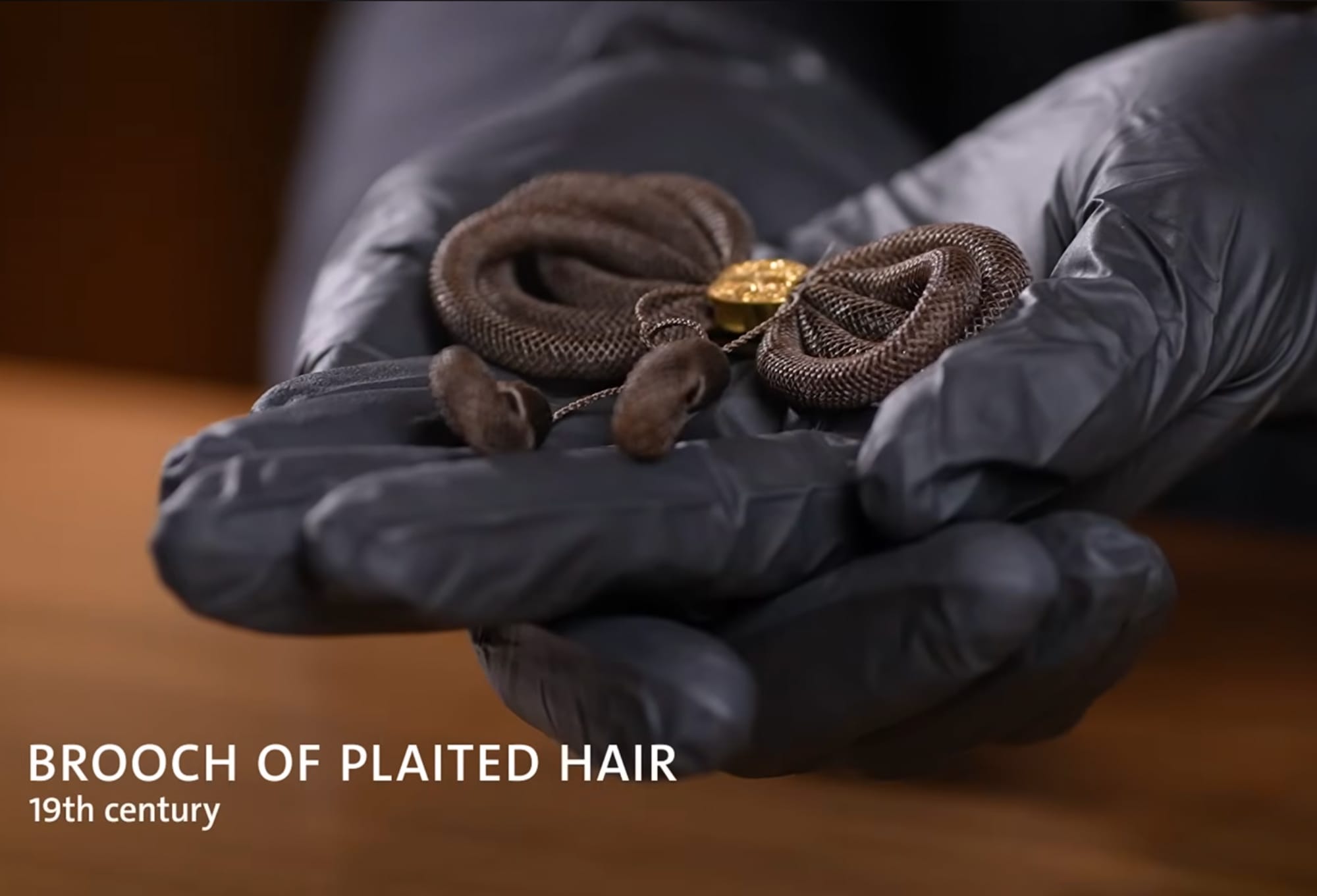 a still of hands holding a brooch made of hair